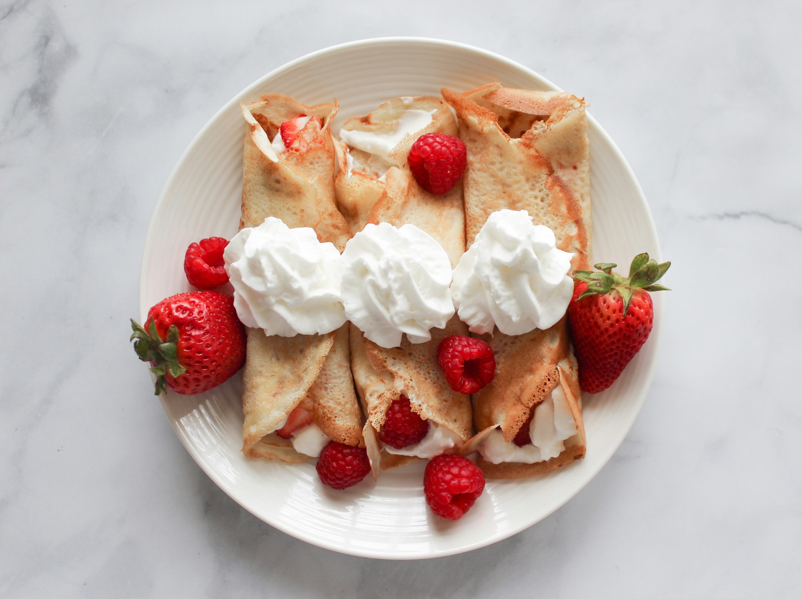 Three crepes topped with strawberries and whipped cream