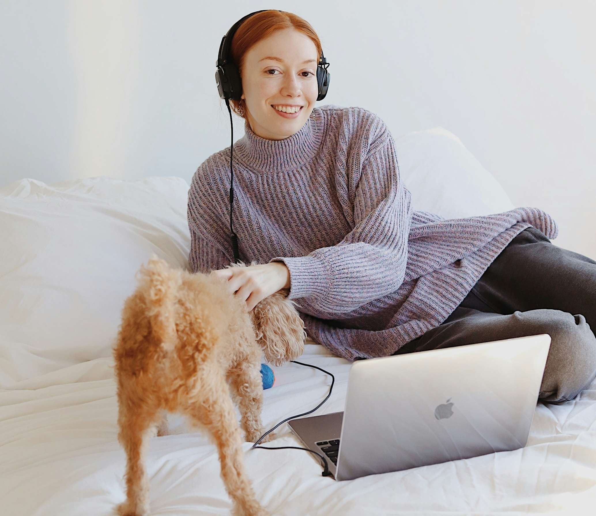 Woman on bed petting dog with computer in front of her