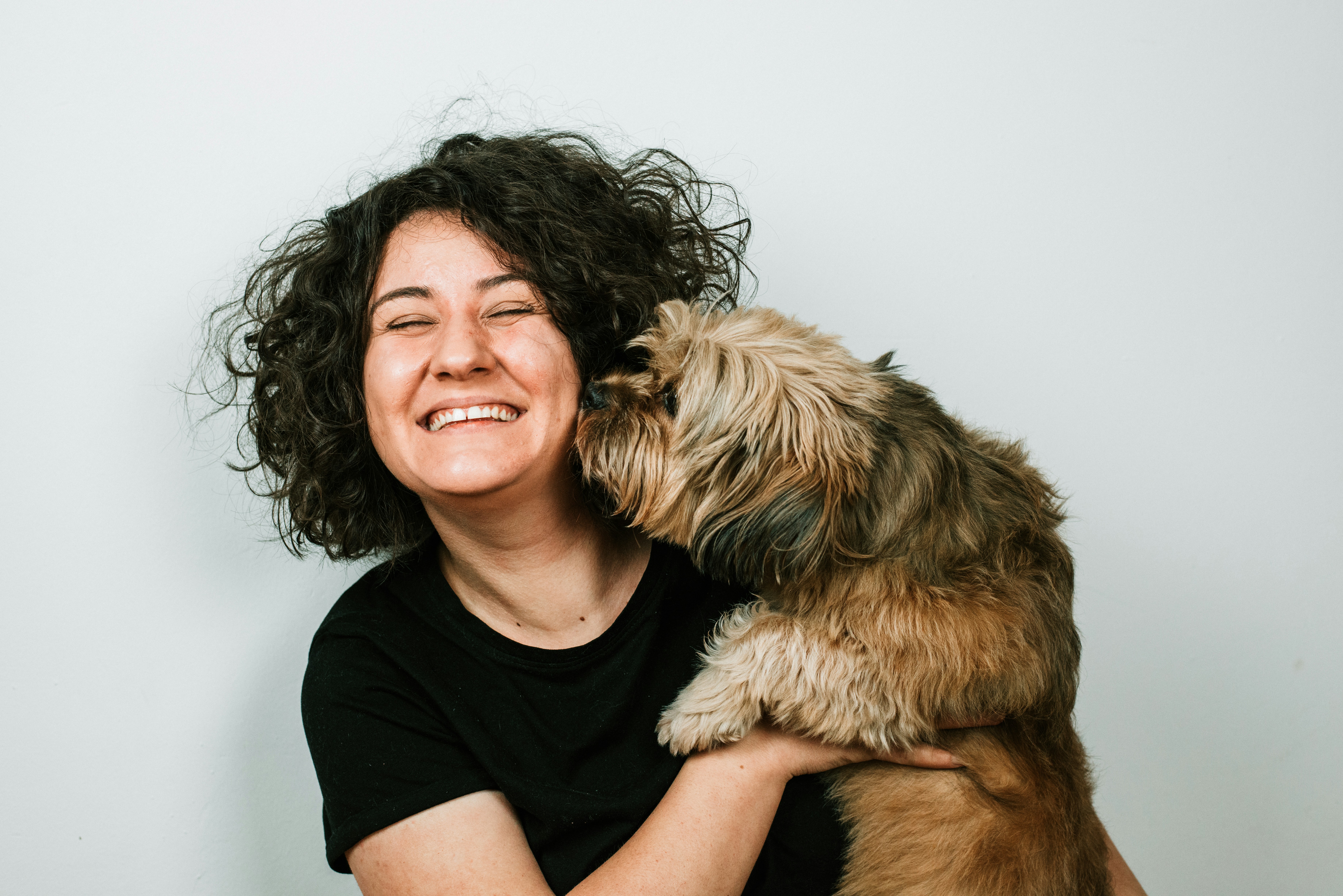 Woman with a smile happy holding a small scruffy dog who is liking the person's face